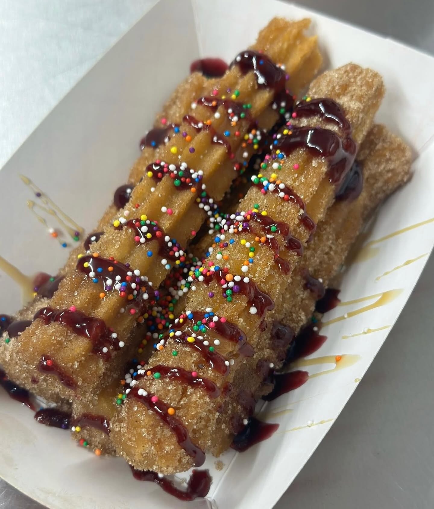 Fresh churros dusted in cinnamon sugar with berry drizzle and sprinkles